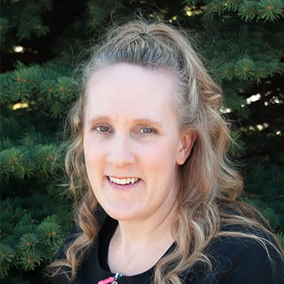Massage Therapist Alicia Smiling Outdoors In Front Of Pine Tree