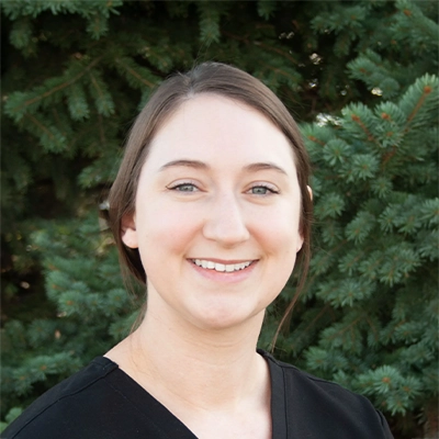Nurse Practitioner Jessica Smiling Outdoors In Front Of Pine Tree