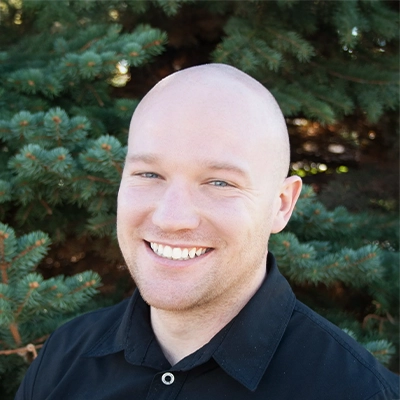 Massage Therapist Kevin Smiling Outdoors In Front Of Pine Tree