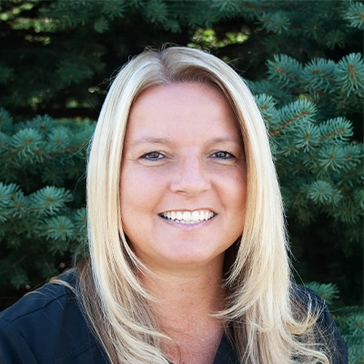 Billing Manager Lisa Smiling Outdoors In Front Of Pine Tree