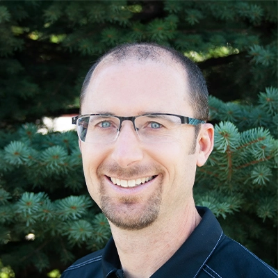 Chiropractor Brian Tolman Smiling Outdoors In Front Of Pine Tree