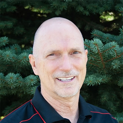 Chiropractor Richard Amon Smiling Outdoors In Front Of Pine Tree