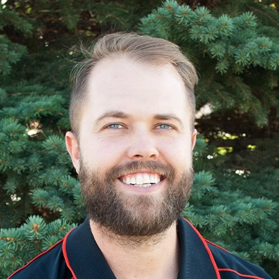 Chiropractor Tyson Stromberg Smiling Outdoors In Front Of Pine Tree